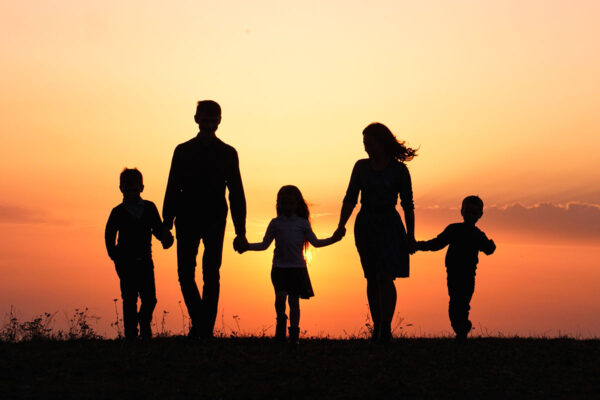 Silhouettes of happy family holding the hands in the meadow during sunset.